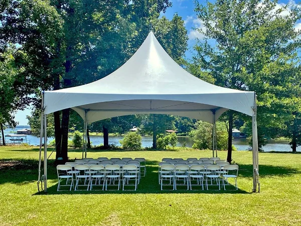 A large white event tent set up on a grassy lawn with rows of white folding chairs arranged underneath.