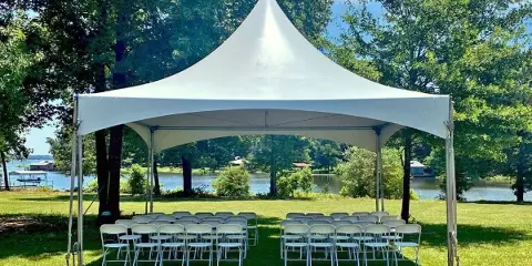 A large white event tent set up on a grassy lawn with rows of white folding chairs arranged underneath.