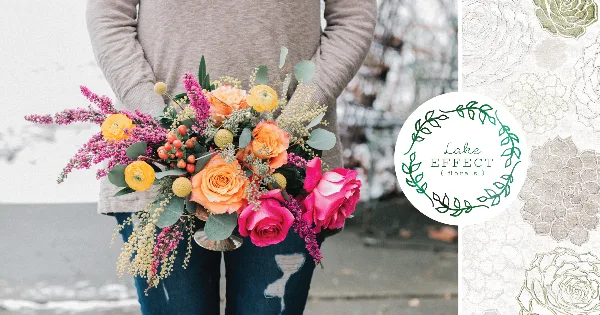A person holding a colorful hand-tied bouquet of orange roses, pink flowers, and greenery.