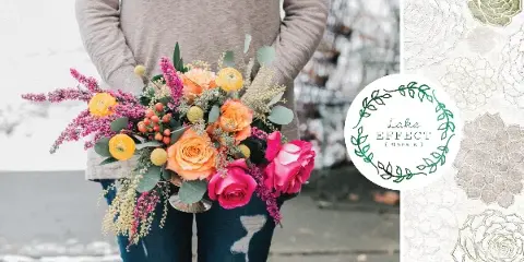 A person holding a colorful hand-tied bouquet of orange roses, pink flowers, and greenery.