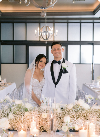 A bride and groom standing at a decorated wedding reception table with white floral arrangements and candles.