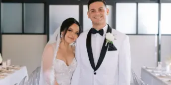A bride and groom standing at a decorated wedding reception table with white floral arrangements and candles.