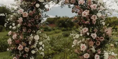 A large outdoor wedding archway decorated with lush greenery, dusty pink roses, and white flowers.