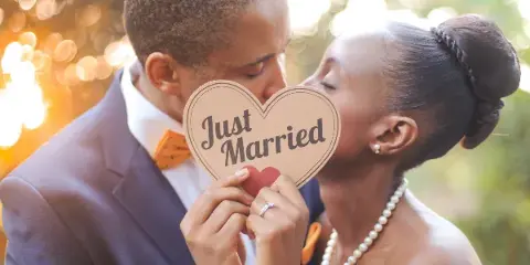 A bride and groom holding a 'Just Married' sign outdoors.