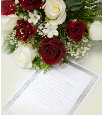 A close-up of a wedding bouquet with red and white roses and baby's breath resting on a wedding invitation.