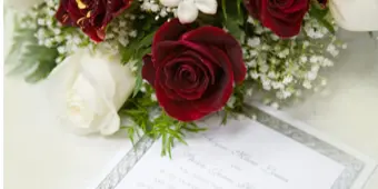 A close-up of a wedding bouquet with red and white roses and baby's breath resting on a wedding invitation.