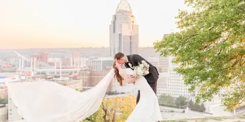 A bride and groom sharing a kiss on a hilltop with the Cincinnati city skyline in the background.