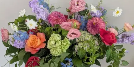 A colorful floral arrangement featuring roses, dahlias, and hydrangeas in a glass vase on a wooden table.