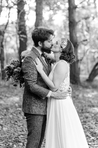Black and white photograph of a bride and groom kissing in a forest setting.