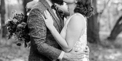 Black and white photograph of a bride and groom kissing in a forest setting.