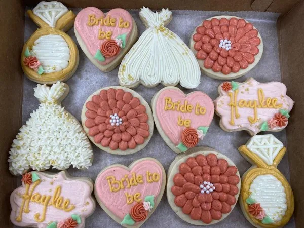 Box of decorated sugar cookies shaped like wedding rings, wedding dresses, and hearts reading 'Bride to be' and 'Haylee'.