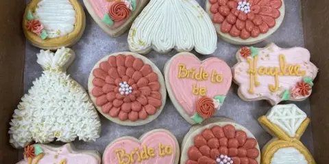 Box of decorated sugar cookies shaped like wedding rings, wedding dresses, and hearts reading 'Bride to be' and 'Haylee'.