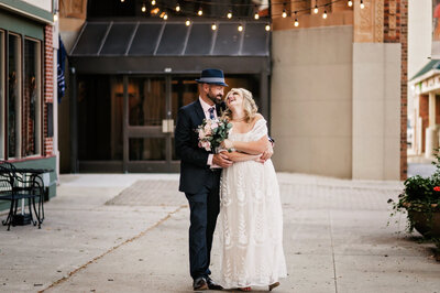 A bride and groom standing together in a wedding dress and suit on a city street.