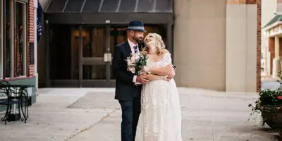 A bride and groom standing together in a wedding dress and suit on a city street.