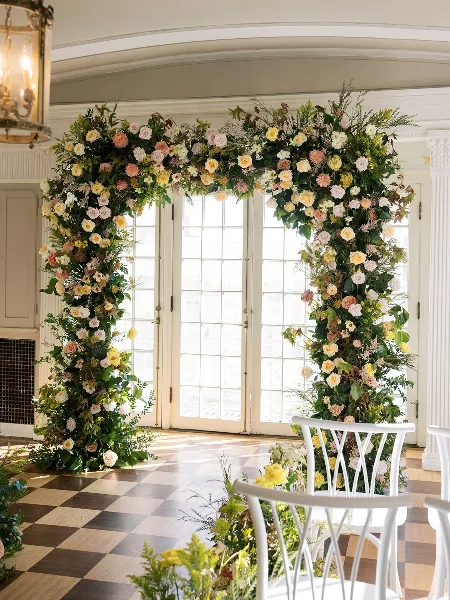 A large floral archway installation featuring roses and greenery in a venue with checkered floors.
