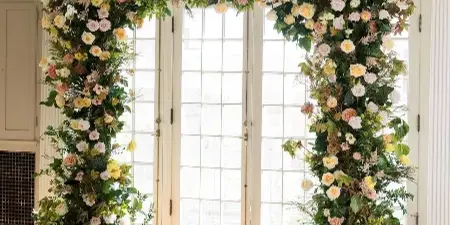 A large floral archway installation featuring roses and greenery in a venue with checkered floors.