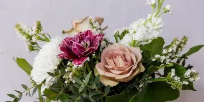 A mixed bouquet of white, pink, and mauve flowers with greenery in a glass jar labeled Habitat Floral Studio on a wooden table.