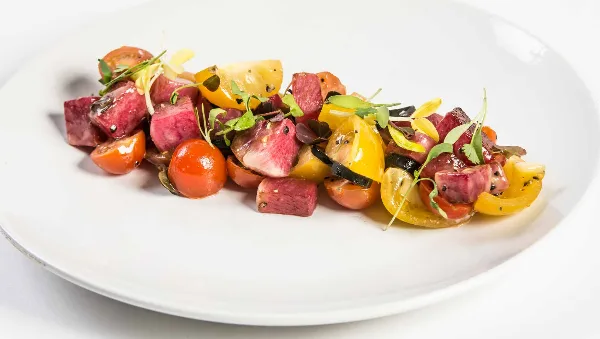 A plated dish of roasted beets and heirloom tomatoes garnished with microgreens on a white plate.
