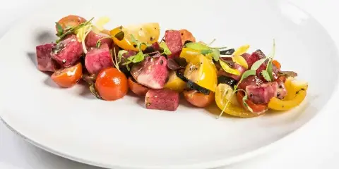 A plated dish of roasted beets and heirloom tomatoes garnished with microgreens on a white plate.