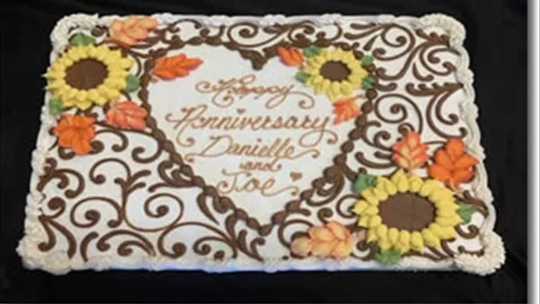 A decorated sheet cake featuring piped brown swirls, yellow sunflowers, and orange leaves with the text 'Happy Anniversary Danielle and Joe'.