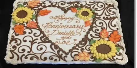 A decorated sheet cake featuring piped brown swirls, yellow sunflowers, and orange leaves with the text 'Happy Anniversary Danielle and Joe'.