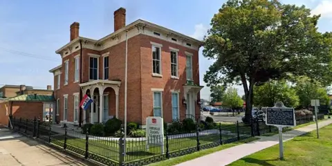 Exterior view of the Bartholomew County Historical Society museum building, a two-story red brick structure with a white sign in the front yard.