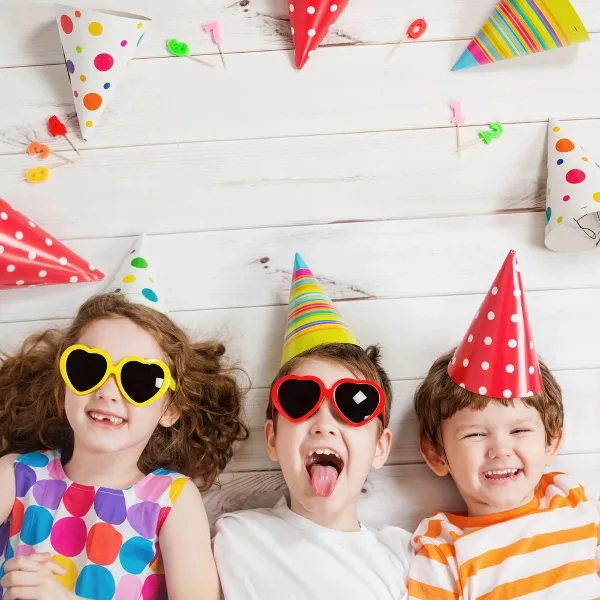 Three children wearing party hats and sunglasses at a party.