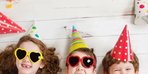 Three children wearing party hats and sunglasses at a party.