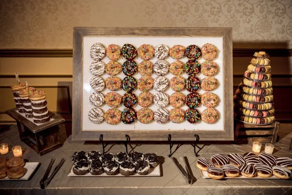 A styled event dessert table featuring a framed donut wall, a macaron tower, and assorted pastries.
