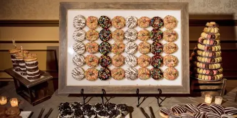 A styled event dessert table featuring a framed donut wall, a macaron tower, and assorted pastries.