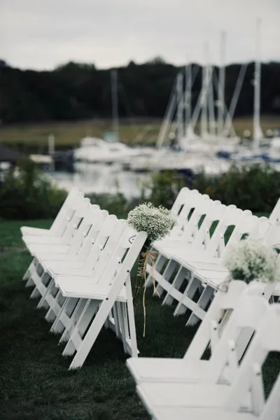 Rows of white folding chairs arranged on a lawn for an outdoor event, with a marina in the background.