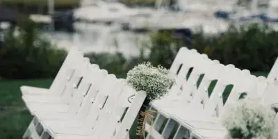 Rows of white folding chairs arranged on a lawn for an outdoor event, with a marina in the background.