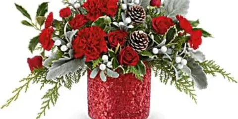 A festive red floral arrangement with carnations, roses, and pinecones in a glittery red vase.