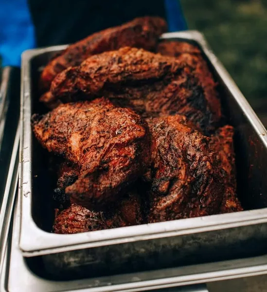 Close-up of smoked BBQ meat pieces in a stainless steel catering pan