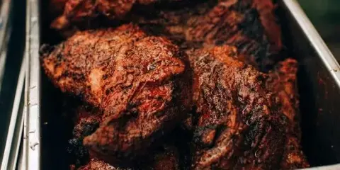 Close-up of smoked BBQ meat pieces in a stainless steel catering pan