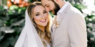 A bride and groom posing together outdoors, with the bride holding a bouquet of white flowers.