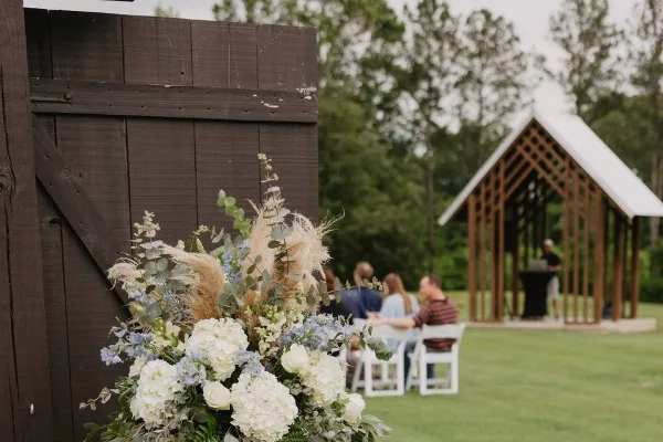 A wedding ceremony taking place outdoors with a wooden gazebo and floral arrangements.