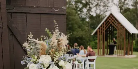 A wedding ceremony taking place outdoors with a wooden gazebo and floral arrangements.