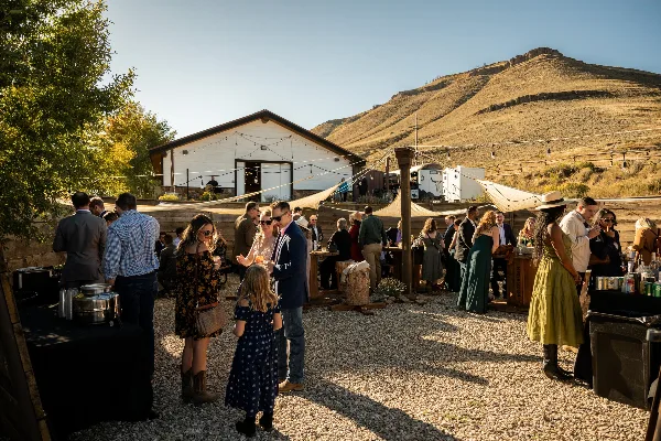 Guests socializing outdoors at a wedding reception in front of a white barn venue with mountain views.