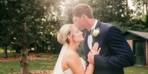 A bride and groom sharing a tender moment outdoors, with the groom kissing the bride's forehead.