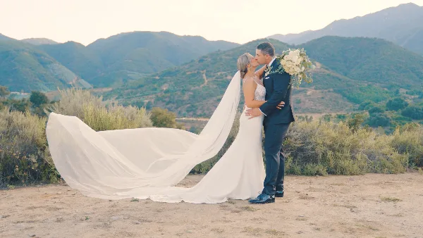 A bride and groom sharing a kiss in a scenic outdoor landscape with mountains in the background.