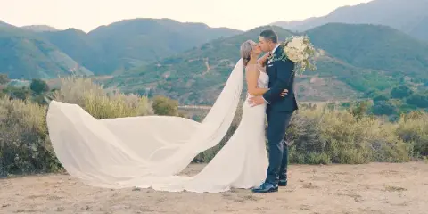 A bride and groom sharing a kiss in a scenic outdoor landscape with mountains in the background.
