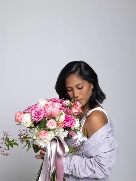 A woman holding a large, custom floral bouquet of pink and white roses and hydrangeas.