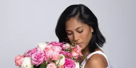 A woman holding a large, custom floral bouquet of pink and white roses and hydrangeas.