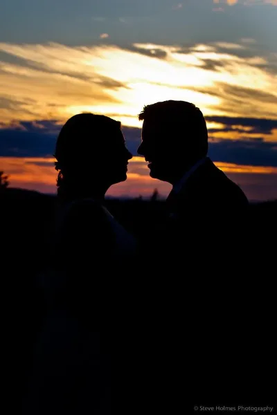 Silhouette of a bride and groom facing each other against a sunset sky.