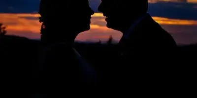 Silhouette of a bride and groom facing each other against a sunset sky.