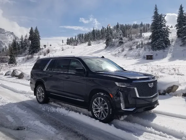 A black Cadillac Escalade SUV parked on a snowy road in a mountainous landscape.