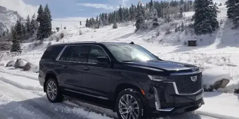 A black Cadillac Escalade SUV parked on a snowy road in a mountainous landscape.