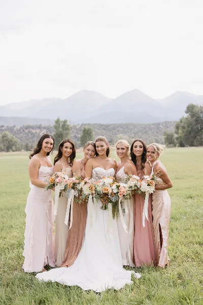A bride and her bridesmaids posing in a grassy field with mountains in the background.