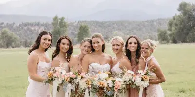 A bride and her bridesmaids posing in a grassy field with mountains in the background.